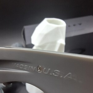 May include: A close-up shot of a grey object with the text "MADE IN U.S.A." embossed on its surface. A white object is in the background. The image is set against a dark background.