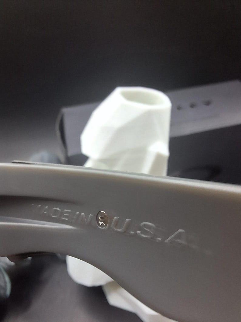 May include: A close-up shot of a grey object with the text "MADE IN U.S.A." embossed on its surface. A white object is in the background. The image is set against a dark background.