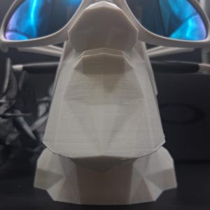 May include: A white, geometric sunglasses display stand holding a pair of sunglasses with blue reflective lenses. The stand has a stylized, angular design. The sunglasses are white with a modern frame.