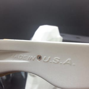 May include: Close-up of a white plastic object with the text "MADE IN U.S.A." embossed on its surface. The object has a curved shape and a small, circular detail near the text. The background is dark.