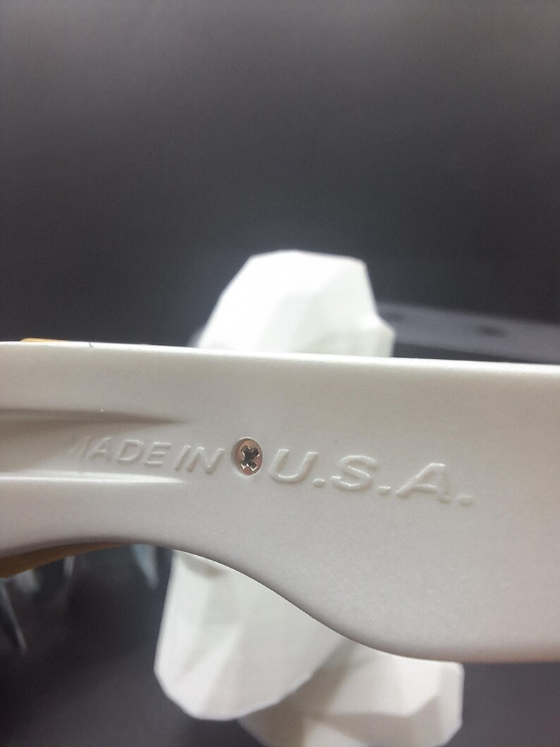 May include: Close-up of a white plastic object with the text "MADE IN U.S.A." embossed on its surface. The object has a curved shape and a small, circular detail near the text. The background is dark.