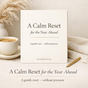 May include: A cream-colored journal titled "A Calm Reset for the Year Ahead" with the tagline "A gentle reset - without pressure." A gold pen rests beside the journal. A cup of coffee and a vase with dried flowers are in the background.