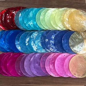 Peut inclure: Une collection de disques en coquillage plats et circulaires disposés en trois rangées horizontales. Les disques présentent une finition nacrée et irisée dans un spectre de couleurs incluant rouge, bleu sarcelle, vert, jaune, bleu, violet et rose.