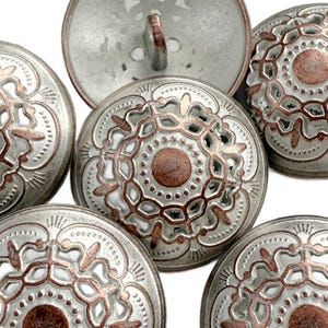May include: A selection of silver metal buttons with an ornate, openwork pattern. Each button has a central copper-coloured circle and detailed designs. The buttons are circular and have a shank for sewing.