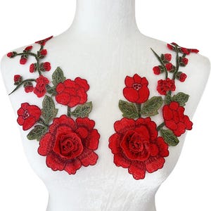May include: Two red embroidered floral appliques. Each applique features large, detailed red roses with green leaves and smaller red buds. The appliques are designed to be sewn onto fabric, adding a decorative floral element.