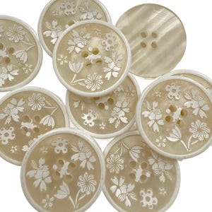 Puede incluir: Una colección de botones color crema con un diseño floral. Cada botón tiene un borde blanco y cuatro agujeros para coser. El patrón floral está grabado en la superficie del botón.