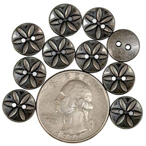May include: A collection of antique silver-toned buttons with a floral design, each featuring two holes for sewing. The buttons are arranged around a U.S. quarter for size comparison. The quarter is dated 1977.