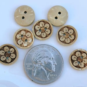 May include: A collection of beige buttons with a floral design and two or four holes. The buttons are next to a U.S. quarter coin for size comparison. The buttons have a light brown floral pattern.