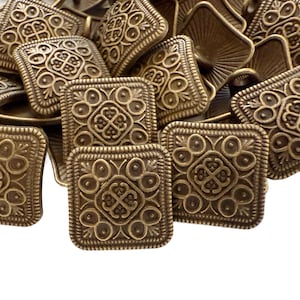 May include: A collection of antique brass-colored square buttons with ornate, symmetrical designs. Each button features a raised floral or geometric pattern within a square frame, creating a vintage aesthetic. The buttons are piled together, showcasing their intricate details.