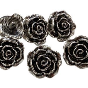 May include: Six antique silver-toned rose-shaped buttons. The buttons have detailed petals and a vintage aesthetic. One button has a mesh backing with a shank. These decorative buttons are ideal for sewing and craft projects.