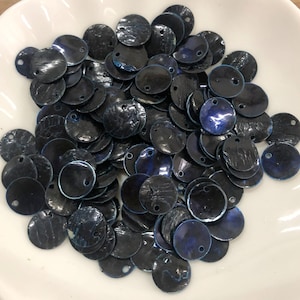 May include: A collection of small, circular, dark blue shell discs, each featuring a single pre-drilled hole near the edge. These flat, iridescent components exhibit a natural, textured surface with subtle variations in deep blue and black tones.