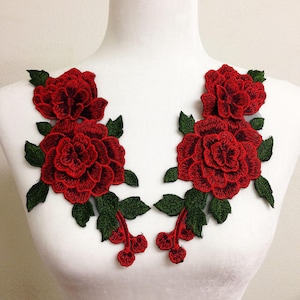 May include: Two red embroidered rose appliques with green leaves. The floral patches feature detailed stitching and are designed to be sewn onto fabric. The appliques are displayed on a white mannequin.