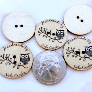 May include: A collection of wooden buttons with two holes each. Some buttons feature an owl design with the text "Handmade by Nola Crosby". A U.S. quarter is included for size reference.
