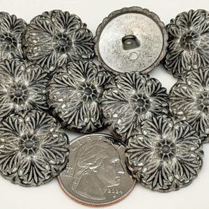 May include: A collection of silver-toned metal buttons with a floral design. The buttons are arranged on a white surface, with a US quarter coin for size comparison. The buttons have a detailed, textured appearance.
