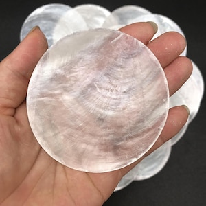 May include: A collection of circular, translucent white mother-of-pearl shell discs. Each disc features a smooth, flat surface with a natural iridescent sheen and visible concentric growth rings, showcasing the organic texture of the shell material.