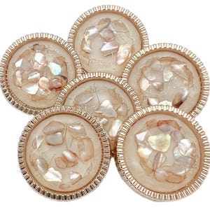 May include: A cluster of six round, decorative buttons. Each button features a cream-colored center filled with iridescent, shell-like fragments. The buttons are framed by a gold-colored, ridged border, creating a luxurious appearance.