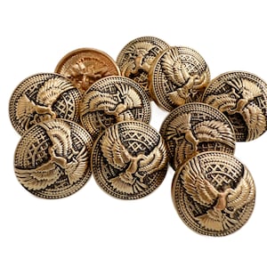 Può includere: Una collezione di bottoni antichi color ottone. Ogni bottone presenta un design dettagliato di un uccello con le ali spiegate, circondato da motivi intricati. I bottoni sono rotondi e hanno un leggero rilievo, che conferisce loro un aspetto vintage.