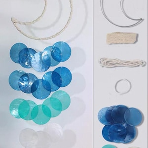 May include: A DIY mobile kit featuring a crescent moon frame wrapped in off-white cord, accompanied by circular blue, teal, and translucent shell discs. The set includes a metal moon frame, lace trim, white cord, a ring, and loose shell pieces.