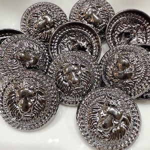 Peut inclure: Ensemble de boutons argentés foncés ornés d'une tête de lion détaillée. Les boutons ronds présentent un relief en forme de tête de lion entourée d'une crinière texturée. Idéal pour les vêtements ou les projets d'artisanat.