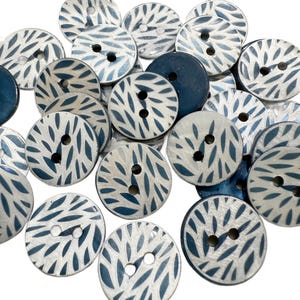 May include: A collection of round buttons with a two-hole design. The buttons are primarily white with a blue leaf-like pattern. Some buttons are solid navy blue. These decorative buttons are ideal for sewing and craft projects.