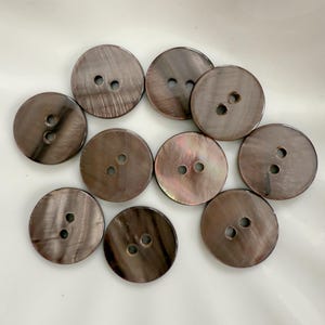 May include: Ten round, dark brown buttons with two holes each. The buttons have a pearlescent sheen, with subtle variations in colour and texture. Suitable for sewing projects, these buttons offer a classic and elegant appearance.