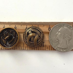 May include: Three antique brass buttons and a quarter coin are displayed on a wooden ruler. The buttons feature intricate designs, including an anchor and a woven pattern. The quarter is dated 1972.