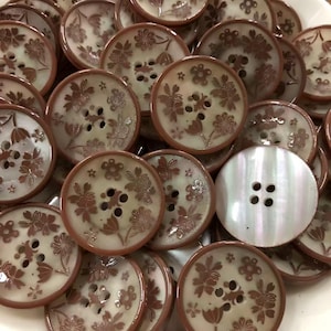 May include: A collection of round, four-hole buttons featuring a cream-colored base with a brown floral pattern and a brown rim. One button is plain, iridescent white with four holes. The buttons have a smooth, glossy finish and varied designs.