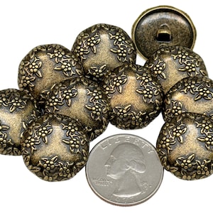 May include: A collection of antique brass-colored buttons with a floral design. The buttons are round with a slightly domed shape and a detailed embossed pattern. A US quarter is included for size reference.
