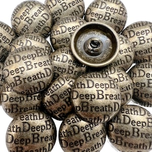 May include: A collection of antique bronze-colored snap buttons. Each button is round and embossed with the words "Deep Breath" in a repeating pattern. The buttons have a vintage, weathered appearance.