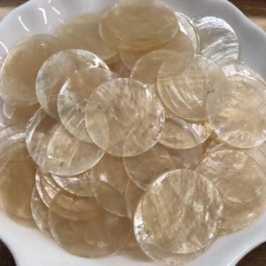 Peut inclure: Une collection de disques circulaires en nacre, translucides et blanc cassé. Chaque disque plat et fin présente une surface lisse et irisée avec un éclat nacré naturel et de petits trous pré-percés pour la fixation ou l'enfilage.