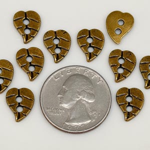 May include: A collection of antique brass-colored leaf-shaped buttons with two holes for sewing. A U.S. quarter coin is included for size comparison. The buttons have a detailed leaf vein design.