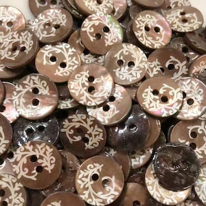 May include: A collection of round, brown mother-of-pearl buttons, each featuring two center holes and a white, etched, swirling vine pattern. The buttons have a smooth, iridescent finish with varying shades of brown, ranging from light to dark.