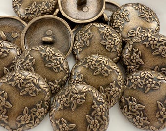 May include: A collection of antique bronze-colored buttons. Each button is round with a floral design around the edges and a loop on the back for sewing. The buttons are approximately 1 inch in diameter.