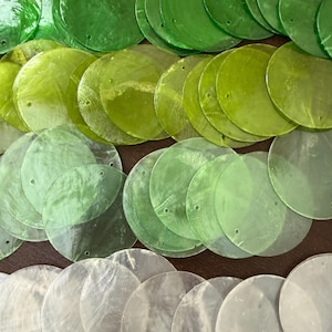 May include: A collection of circular, flat, translucent discs arranged in rows. The discs feature a gradient of colors ranging from deep emerald green at the top, transitioning to lime green, pale mint, and finally clear, colorless pieces at the bottom.