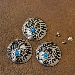 May include: Three circular silver-toned metal buttons featuring a raised profile of a person wearing a feathered headdress. Each button is accented with a small, round, bright blue turquoise-colored stone at the temple. Two small metal screws are included.