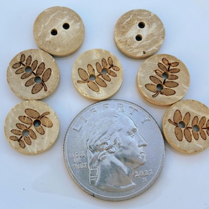 May include: A collection of eight natural-toned wooden buttons. Some buttons have two holes, while others feature a leaf design. A quarter coin is included for size reference. The buttons are round and have a light brown color.