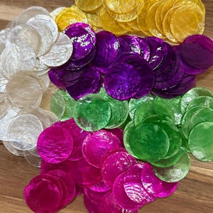 May include: A collection of circular, translucent capiz shell discs in a vibrant assortment of colours including white, yellow, purple, green, and magenta. Each thin, flat disc features a natural, iridescent, and slightly textured surface finish.