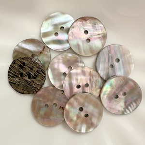 May include: A collection of iridescent, round buttons with two or four holes. The buttons vary in color, with shades of white, pink, and brown. One button has a dark, textured appearance. These buttons are ideal for sewing and craft projects.