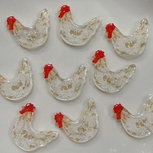 Puede incluir: Nueve botones transparentes con forma de gallina, con crestas rojas y detalles amarillos. Los botones tienen un acabado nacarado y dos agujeros para coser. Estos botones decorativos son ideales para proyectos de manualidades.