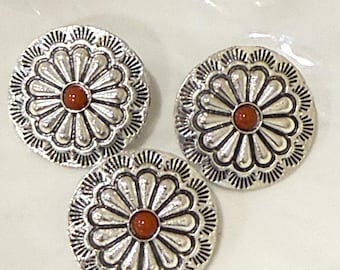 May include: Three circular silver-toned metal buttons featuring a raised floral petal design radiating from a central point. Each button has a small, smooth, reddish-brown circular stone inlay set in the center of the flower pattern.