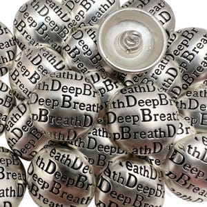 May include: A collection of silver-colored snap buttons. Each button is spherical and embossed with the words "Deep Breath" in a repeating pattern. One button is open, revealing the spring mechanism.