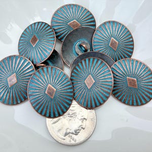 May include: A collection of turquoise and copper-colored metal buttons. Each button has a sunburst design with a diamond-shaped accent in the center. The buttons are approximately 1 inch in diameter.