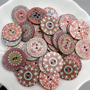 May include: A collection of decorative wooden buttons with intricate floral and geometric patterns in shades of red, pink, green, and blue. Each button has two holes for sewing and a natural wood grain edge. The buttons are arranged in a white bowl.