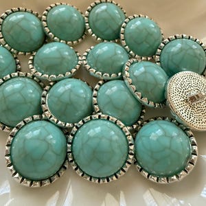 May include: A collection of round buttons featuring a smooth, dome-shaped turquoise surface with a white crackle pattern. Each button is encased in a scalloped silver-toned metal rim, with one button flipped over to reveal a textured silver back and shank.