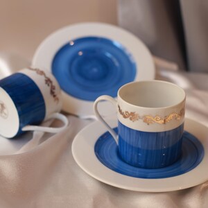 Peut inclure: Deux tasses en porcelaine blanche et deux soucoupes assorties présentant un motif à rayures verticales bleu vif sur la moitié inférieure. Chaque tasse est ornée d'une délicate bande dorée en filigrane près du bord, avec un centre bleu.