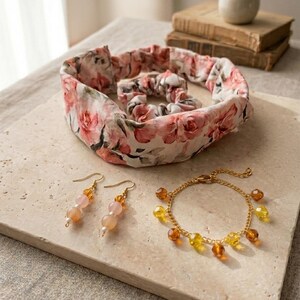 Puede incluir: Un conjunto de accesorios que incluye una diadema floral, una goma para el pelo, pendientes y una pulsera. La diadema y la goma para el pelo presentan un diseño de rosas rosas y blancas. Los pendientes tienen cuentas melocotón y transparentes. La pulsera dorada tiene cuentas ámbar y amarillas.