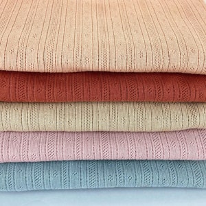 May include: A stack of six fabric swatches in various colours, including beige, red, tan, pink, and blue. The fabric has a textured, waffle-like pattern.