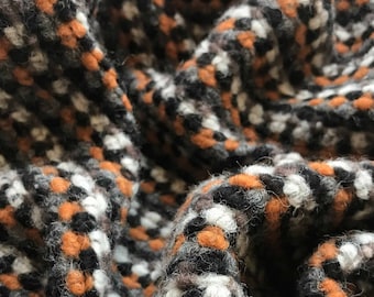 Puede incluir: Primer plano de una tela texturizada con un patrón tejido. La tela presenta una mezcla de colores, incluyendo negro, blanco, naranja y gris. El material parece suave y posiblemente lana o una mezcla de lana.