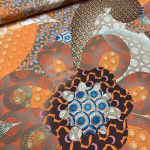 May include: A colorful fabric with a repeating pattern of orange, brown, and blue circles. The fabric has a geometric design and is perfect for quilting, sewing, or crafting.