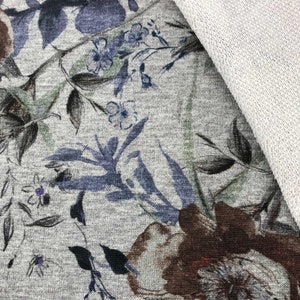 Pode incluir: Close-up de um tecido cinza com estampa floral. O tecido apresenta uma grande flor marrom com um centro branco e flores azuis menores por todo o tecido. O tecido tem uma superfície texturizada.